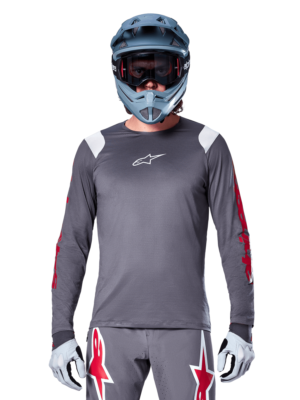 Cycliste VTT portant le maillot à manches longues Alpinestars A-Supra Astar, gris foncé avec graphismes rouges sur les manches et accents blancs aux épaules, pantalon gris assorti avec logos étoiles rouges, casque intégral bleu et masque, équipement de cyclisme tout-terrain coordonné