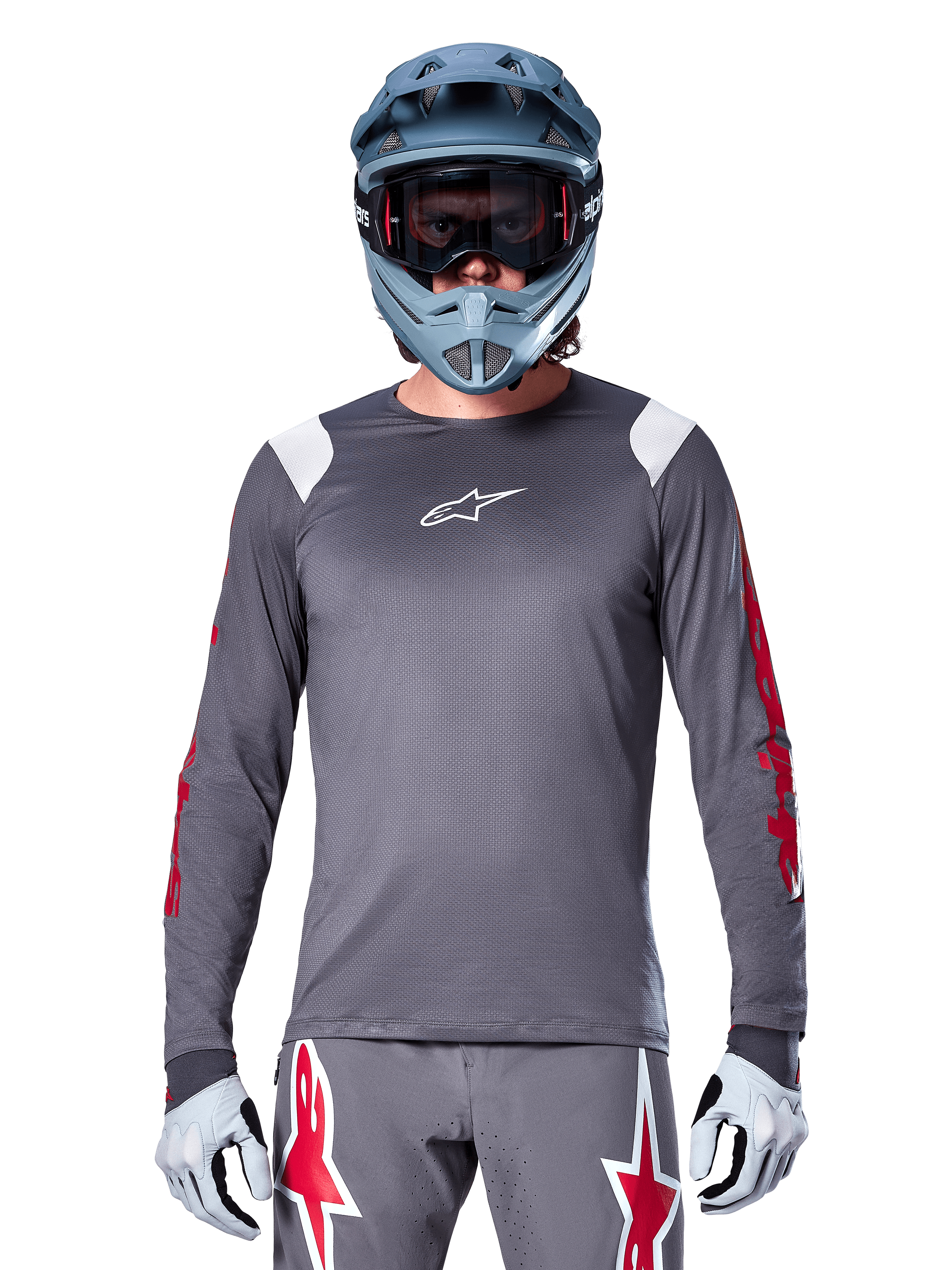 Cycliste VTT portant le maillot à manches longues Alpinestars A-Supra Astar, gris foncé avec graphismes rouges sur les manches et accents blancs aux épaules, pantalon gris assorti avec logos étoiles rouges, casque intégral bleu et masque, équipement de cyclisme tout-terrain coordonné
