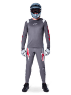 Pilote de VTT portant le maillot à manches longues Alpinestars A-Supra Astar, gris foncé avec des accents rouges et un logo blanc sur la poitrine, pantalon gris assorti avec de grands graphismes d'étoiles rouges, casque intégral bleu avec masque, gants gris clair et chaussures noires, ensemble d'équipement de VTT professionnel