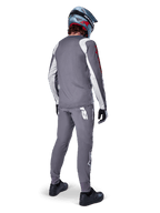 Maillot Alpinestars A-Supra Astar, maillot de VTT à manches longues, gris foncé avec accents blancs sur les manches et logo rouge, vue de dos d'un pilote portant un pantalon gris assorti et un casque intégral bleu, vêtements de cyclisme haute performance