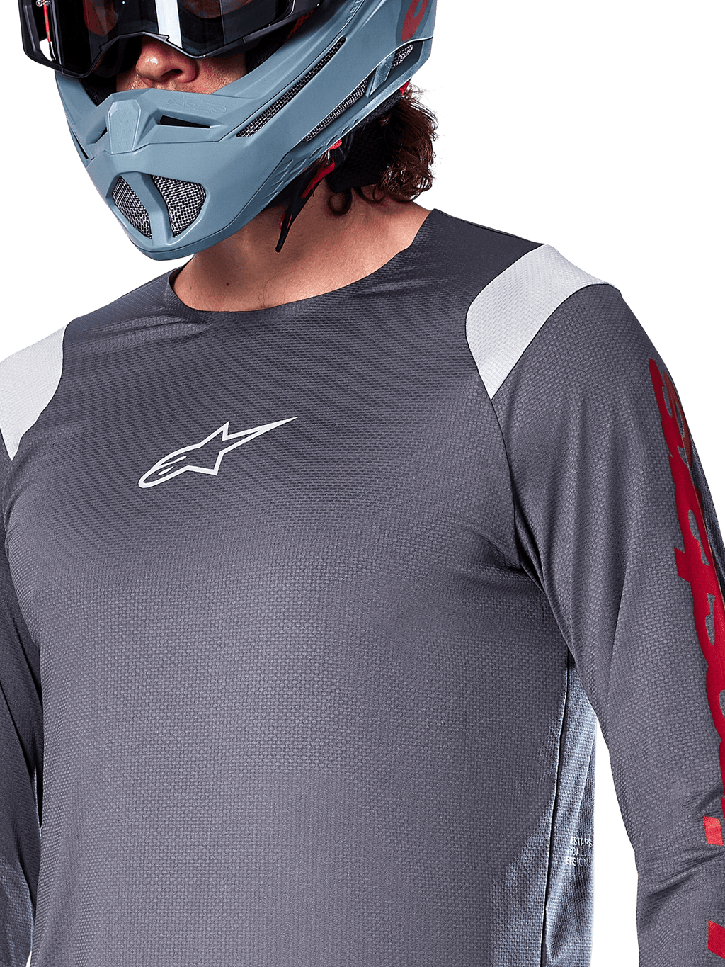 Maillot à manches longues Alpinestars A-Supra Astar, gris foncé avec empiècements blancs aux épaules et graphismes rouges sur les manches, porté avec un casque intégral bleu-gris clair, équipement de VTT haute performance