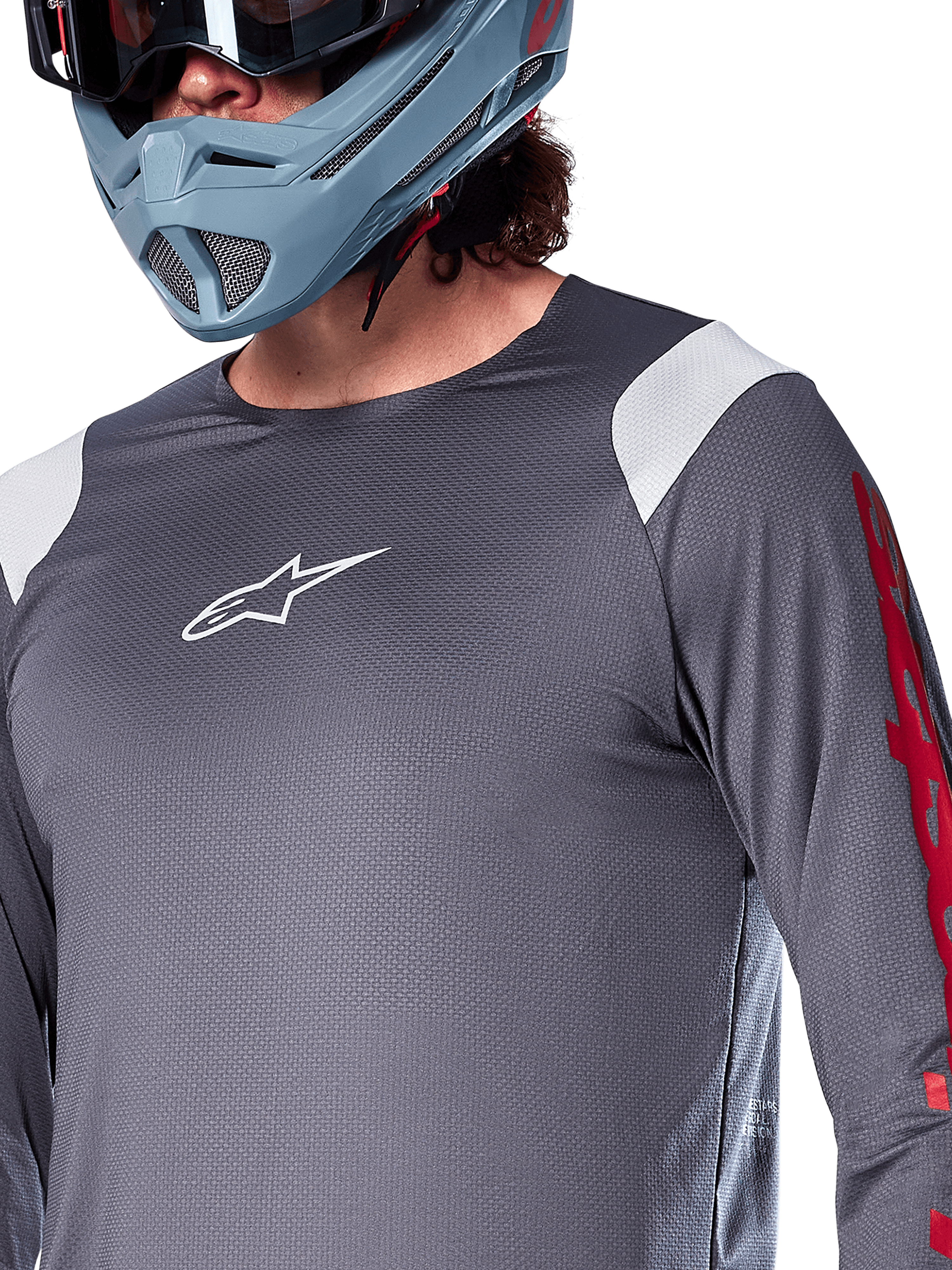 Maillot à manches longues Alpinestars A-Supra Astar, gris foncé avec empiècements blancs aux épaules et graphismes rouges sur les manches, porté avec un casque intégral bleu-gris clair, équipement de VTT haute performance