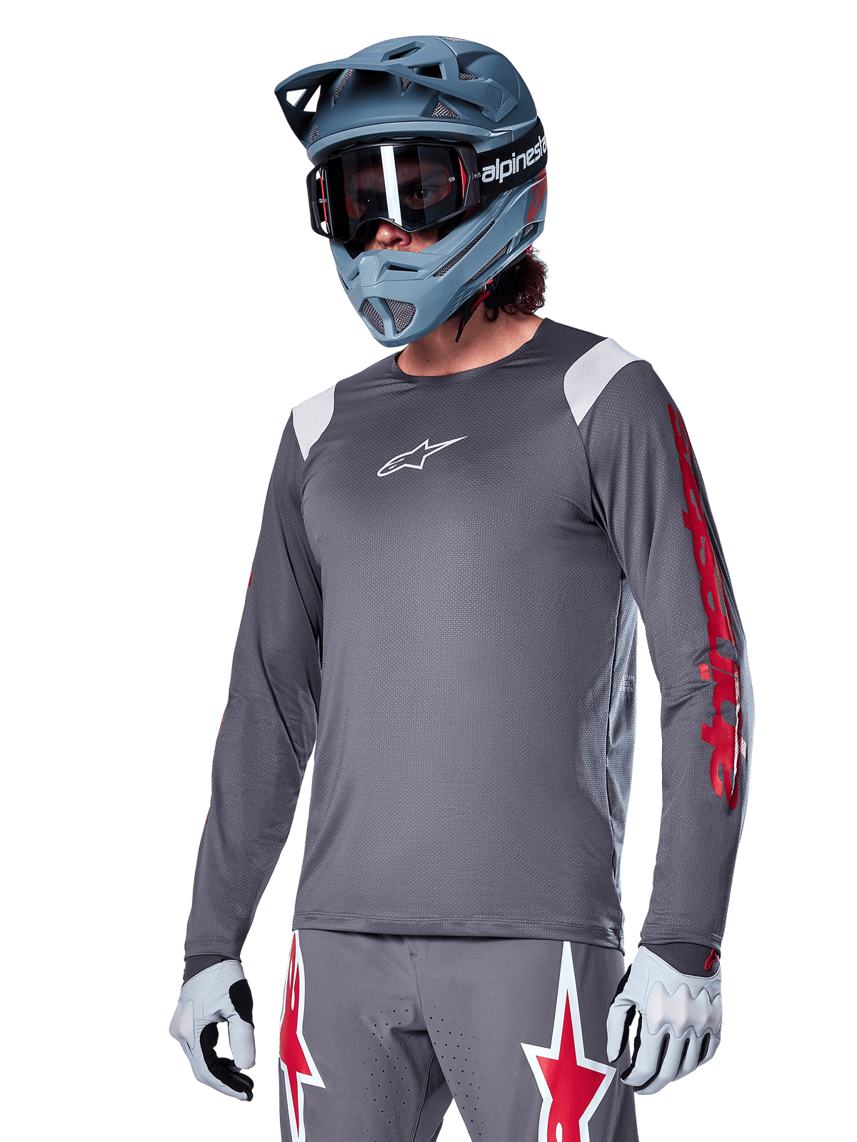 Maillot à manches longues Alpinestars A-Supra Astar, maillot de VTT, gris foncé avec des détails rouges et blancs, coupe performante, porté avec un pantalon gris assorti arborant des graphismes d'étoiles rouges et blanches, tenue de cyclisme tout-terrain complète avec casque intégral et gants
