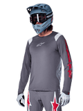 Maillot à manches longues Alpinestars A-Supra Astar, maillot de VTT, gris foncé avec des détails rouges et blancs, coupe performante, porté avec un pantalon gris assorti arborant des graphismes d'étoiles rouges et blanches, tenue de cyclisme tout-terrain complète avec casque intégral et gants