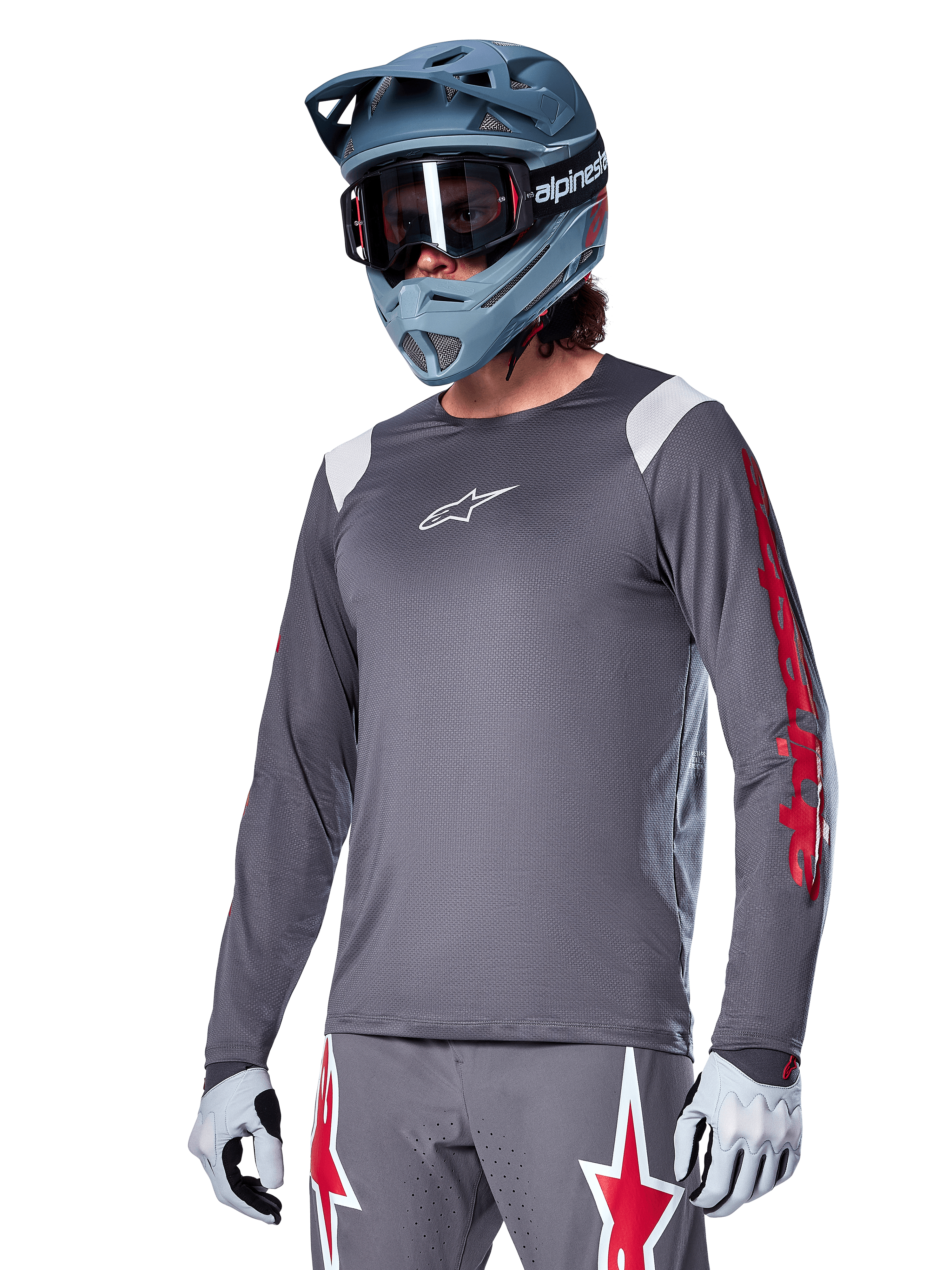 Maillot à manches longues Alpinestars A-Supra Astar, maillot de VTT, gris foncé avec des détails rouges et blancs, coupe performante, porté avec un pantalon gris assorti arborant des graphismes d'étoiles rouges et blanches, tenue de cyclisme tout-terrain complète avec casque intégral et gants