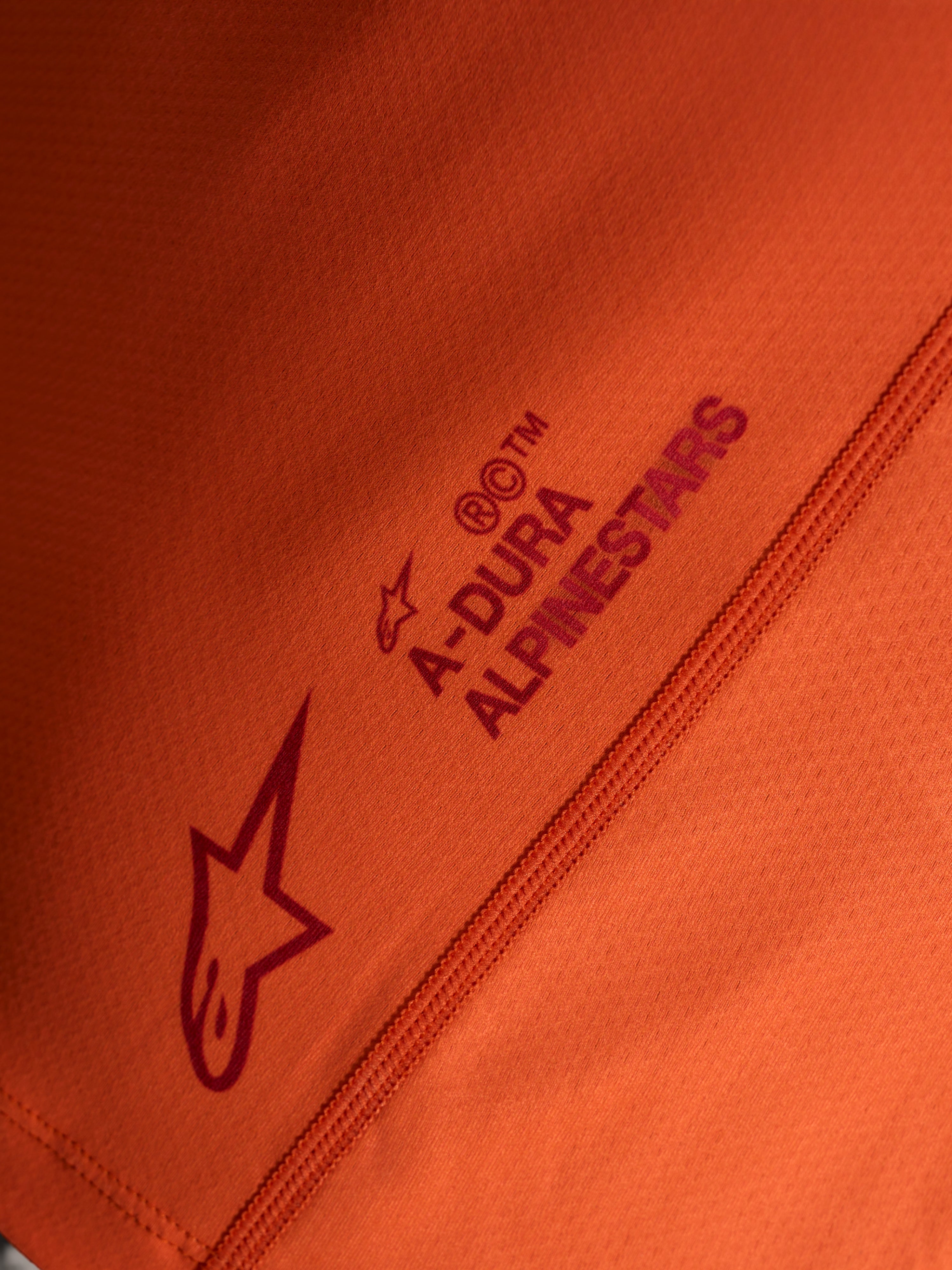 Détail du maillot orange Stella A-Dura Ride, logos Alpinestars et A-DURA sur tissu technique extensible.