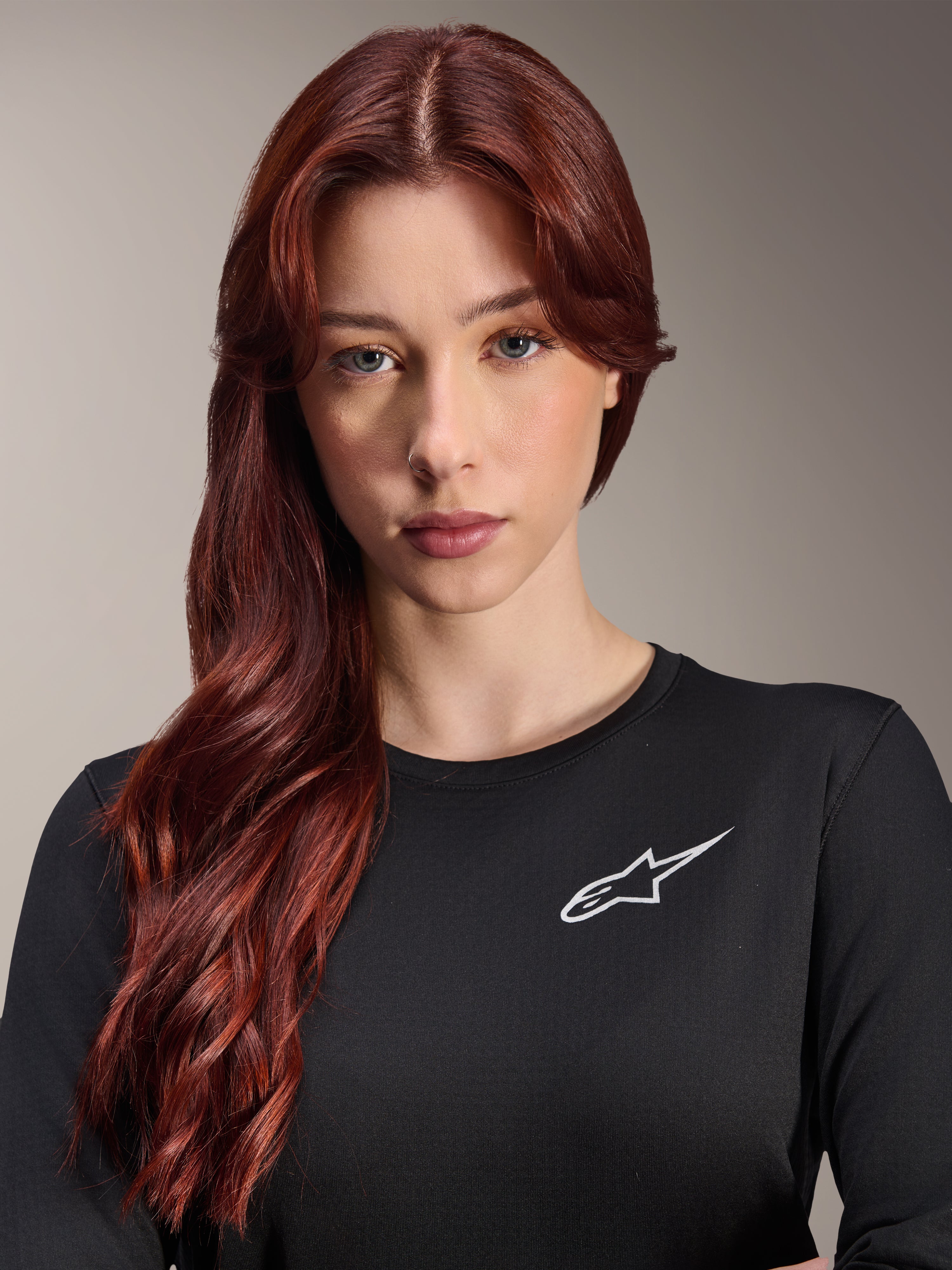 Maillot thermique Alpinestars Stella A-Dura, maillot de VTT à manches longues pour femme, noir avec logo A-star blanc sur la poitrine, portrait rapproché d'une femme aux longs cheveux roux, vêtement de cyclisme pour temps frais