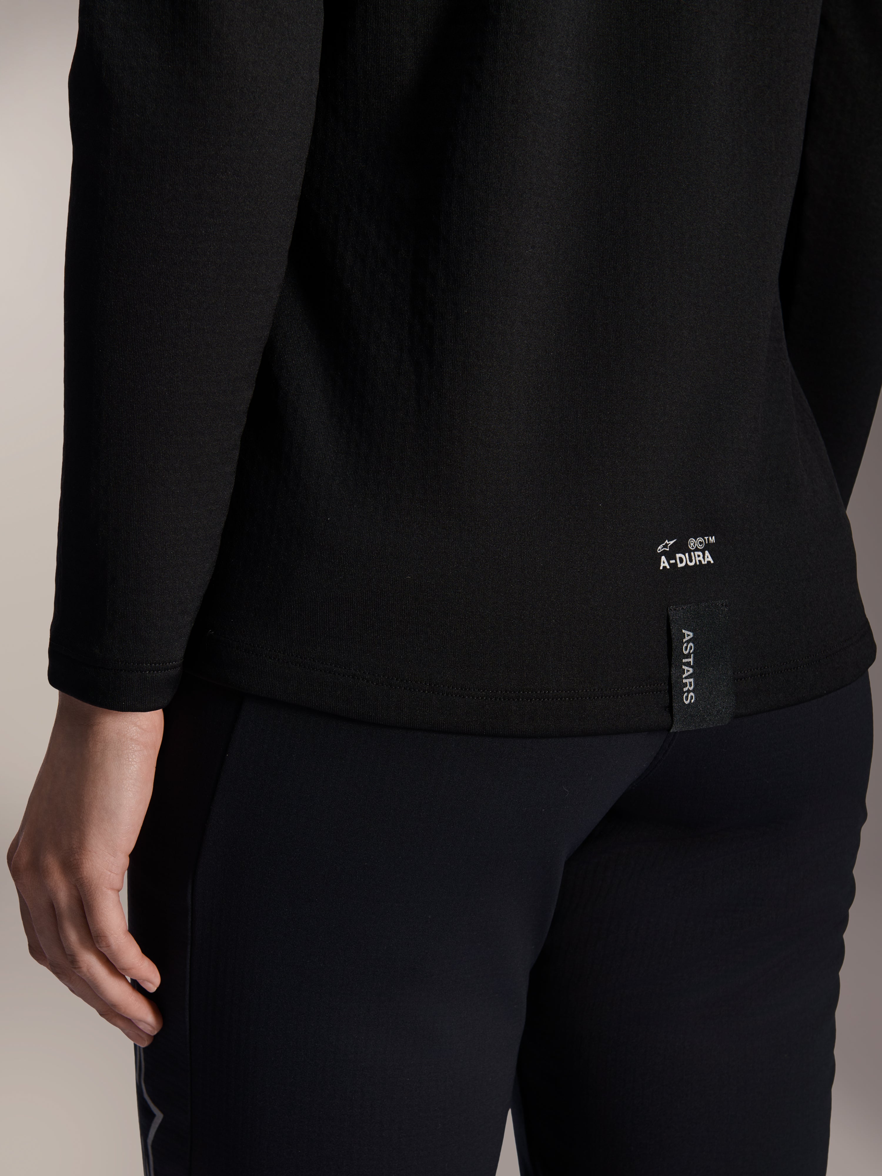 Maillot thermique femme Alpinestars Stella A-Dura, maillot de VTT thermique noir, gros plan sur l'ourlet inférieur arrière avec marquage A-DURA blanc et étiquette logo ASTARS verticale, conçu pour le VTT par temps froid