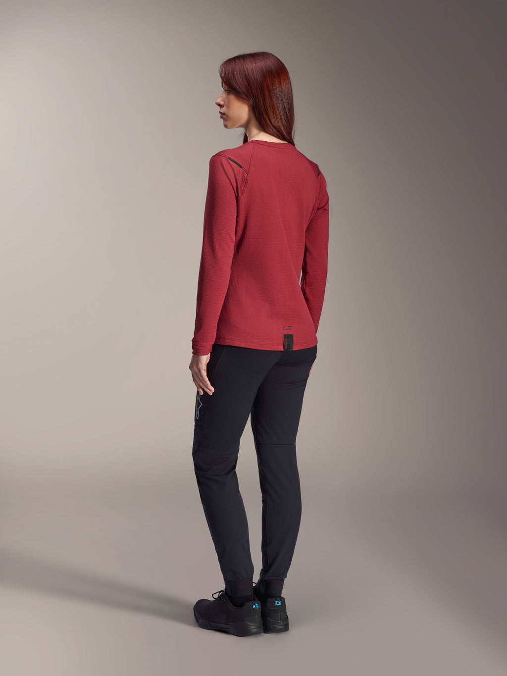 Alpinestars Stella A-Dura Thermal Jersey, Women's long-sleeve mountain bike jersey, Burgundy, back view highlighting the extended drop tail and thermal fabric texture, worn with black MTB pants and black footwear
