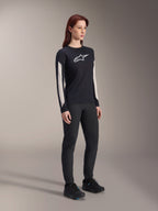 Maillot à manches longues Alpinestars Stella A-Dura Dri Astar pour femme, noir, avec empiècements en maille blanche sur les manches et logo Astar blanc, porté avec un pantalon et des chaussures noirs, vêtement technique de cyclisme pour le VTT