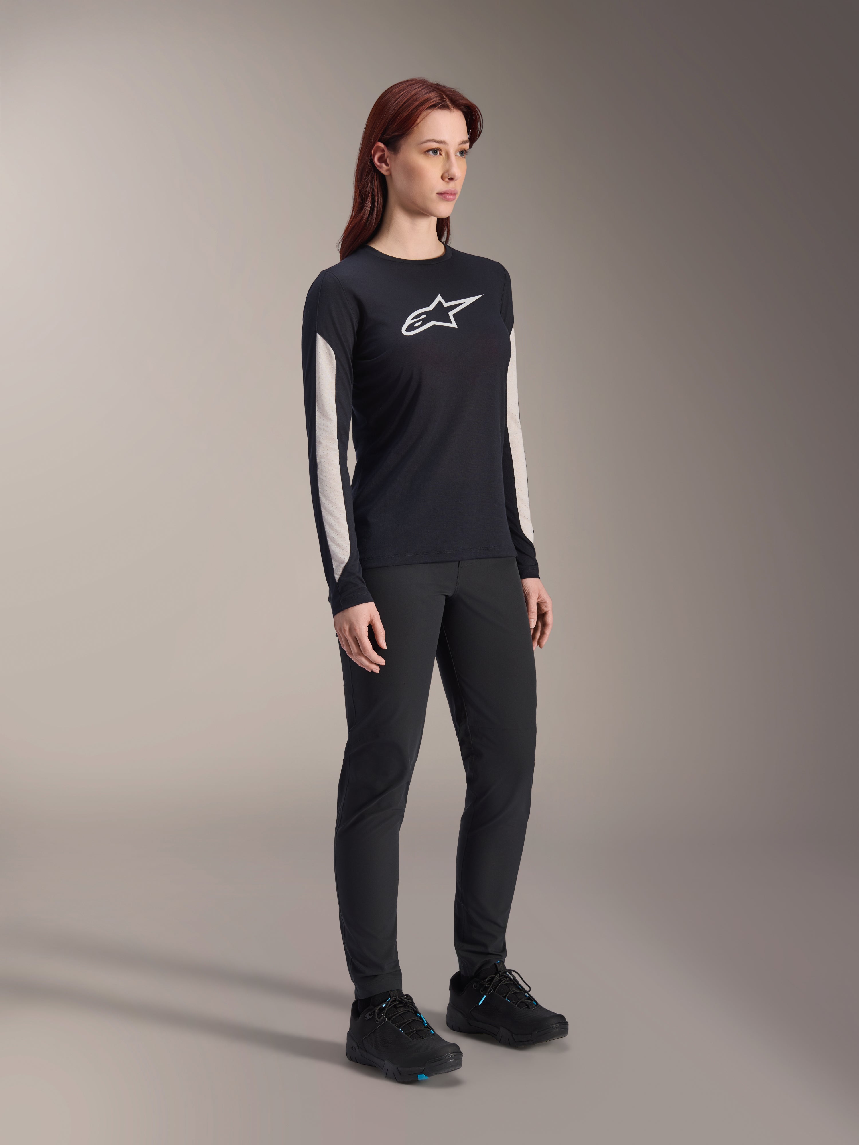 Maillot à manches longues Alpinestars Stella A-Dura Dri Astar pour femme, noir, avec empiècements en maille blanche sur les manches et logo Astar blanc, porté avec un pantalon et des chaussures noirs, vêtement technique de cyclisme pour le VTT