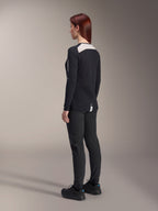 Cycliste portant le pantalon pour femme Alpinestars Stella A-Dura et le maillot Stella A-Dura Elite, noir, vue de dos montrant les empiècements d'épaule en maille blanche sur le maillot à manches longues, pantalon technique à coupe ajustée, équipement de VTT coordonné.