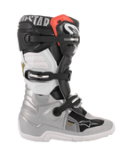 Bottes Alpinestars Youth Tech 7S, bottes de motocross, noir, argent, blanc et doré, vue de profil présentant une coque inférieure argentée, des panneaux supérieurs noirs et blancs, un accent rouge sur le bord supérieur et un système de fermeture à trois boucles.