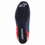 Chaussure de moto Alpinestars Austin, bleu marine et rouge vif, vue de dessous montrant la semelle extérieure en caoutchouc noir avec adhérence texturée ondulée et marquage Alpinestars blanc