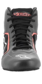 Chaussures Alpinestars Tech-1 K Start V2, chaussures de karting, noir asphalte et orange fluo, vue de face montrant des lacets noirs, le marquage Alpinestars orange sur la languette, le logo étoile blanc sur la pointe et des panneaux en microfibre perforée