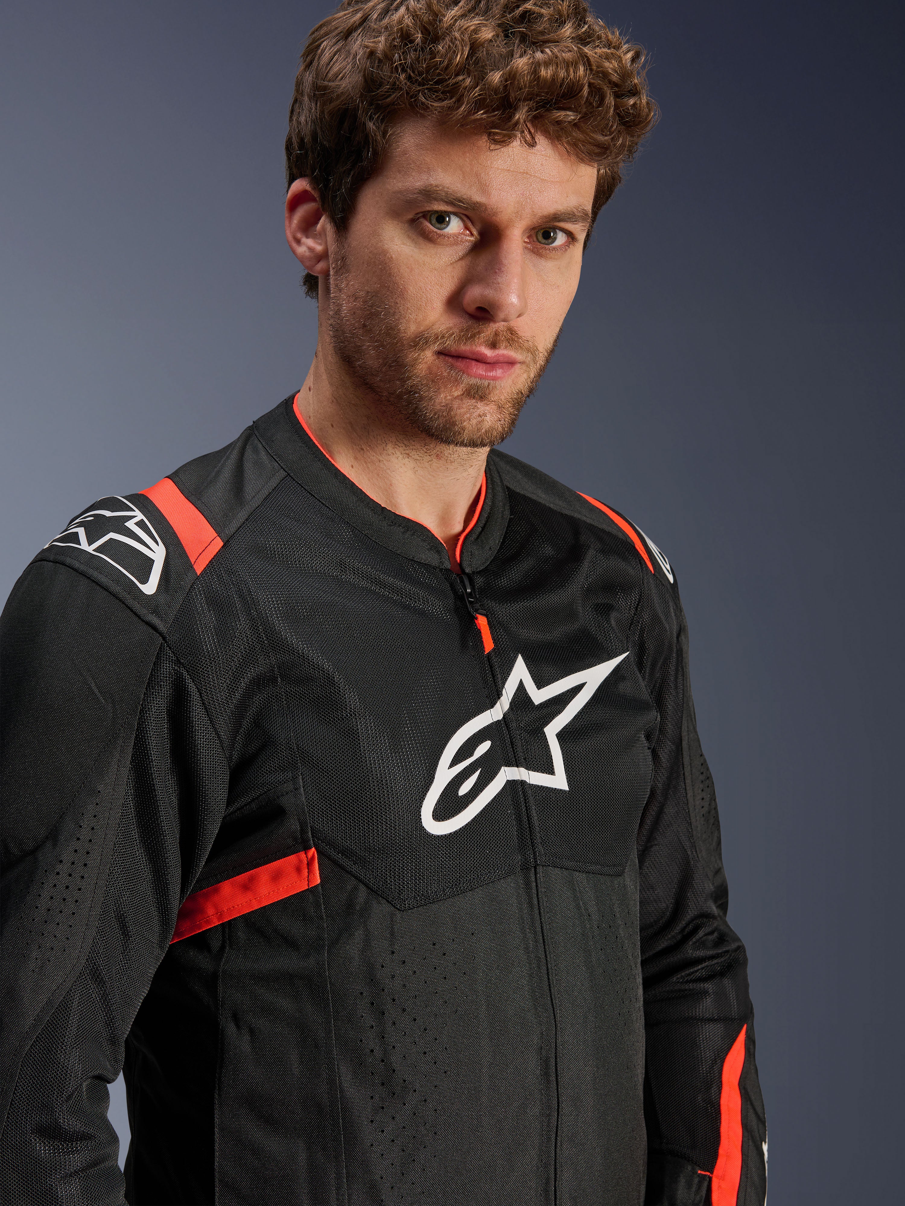 Veste Alpinestars T-Sps Air V2, noire avec des accents rouge fluo, veste de moto en textile mesh, portée par un mannequin, arborant le logo Alpinestars blanc sur la poitrine et les épaules, panneaux en mesh respirant, style urbain sportif