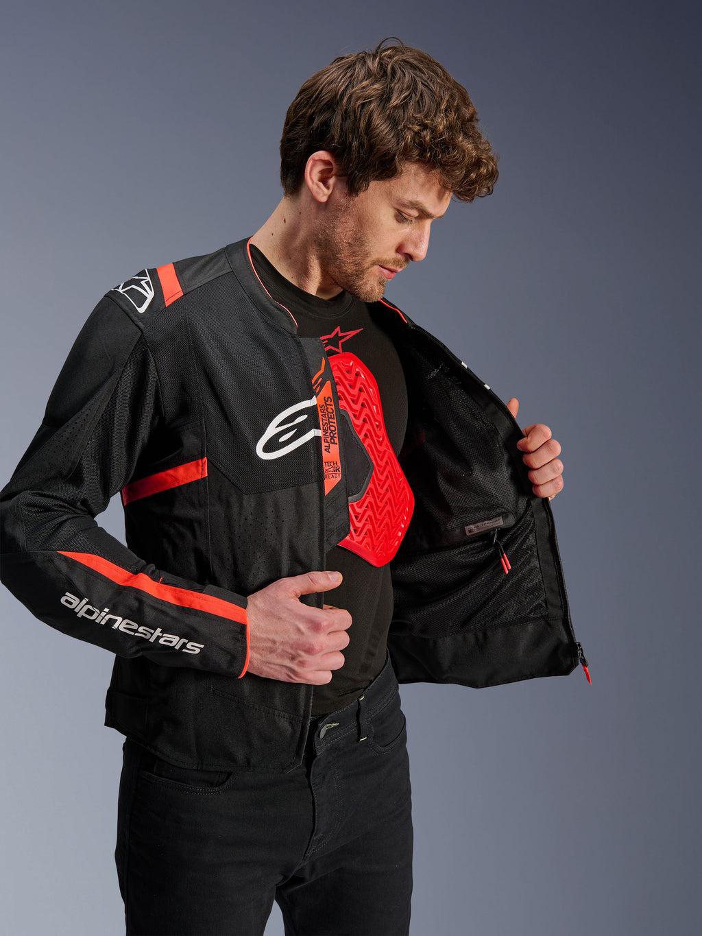 Veste Alpinestars T-Sps Air V2, noir et rouge fluo, portée par un mannequin montrant la doublure en mesh et une protection de poitrine Nucleon rouge, avec logos Alpinestars blancs et panneaux en maille technique