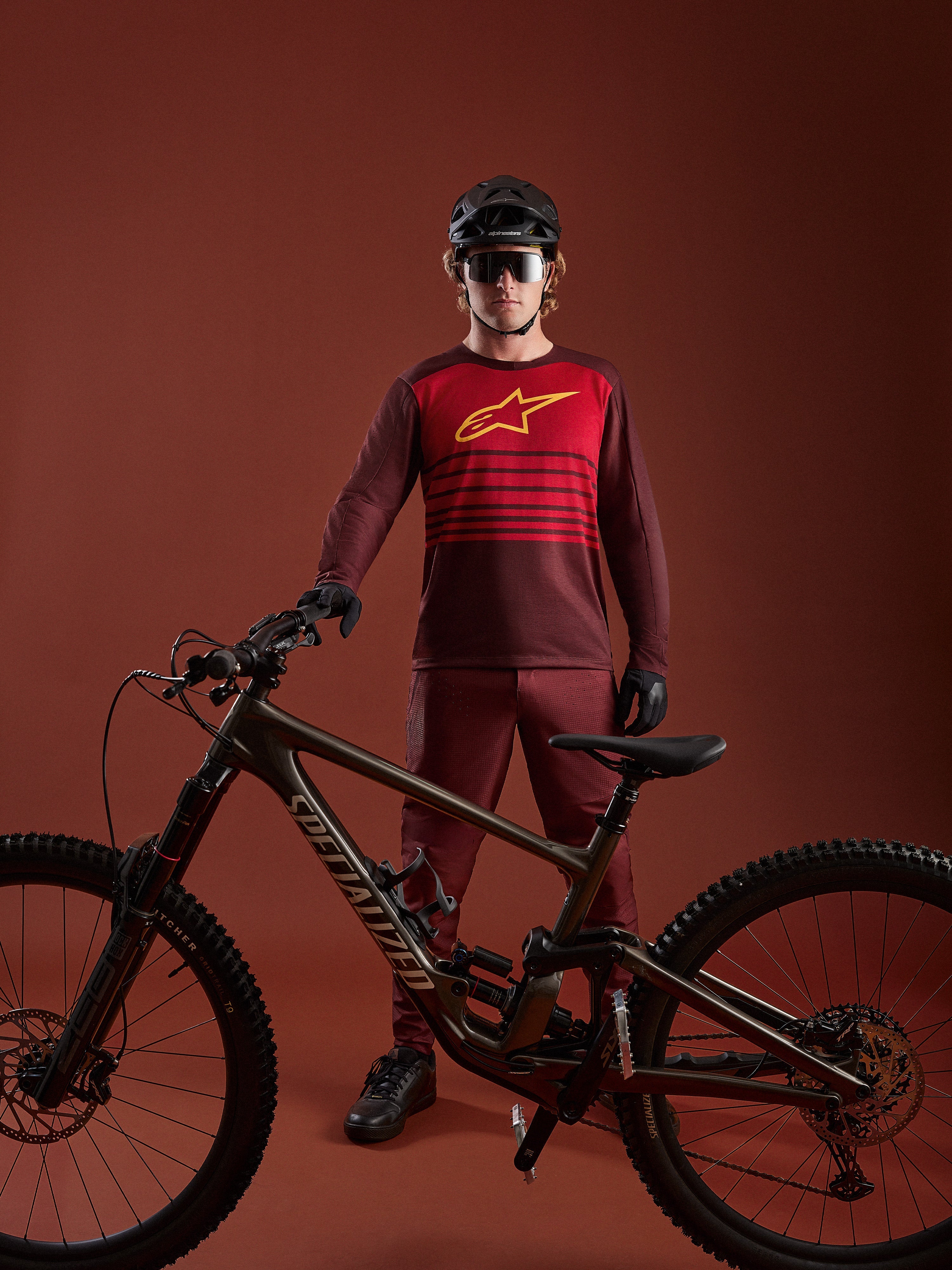 Maillot VTT A-Dura Elite 2.0 bordeaux, manches longues, panneau rouge et logo jaune, présenté avec un VTT.