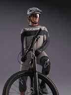 Maillot manches longues Alpinestars A-Dura Race gris, accents noirs, porté par un pilote de VTT équipé.