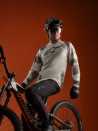 Maillot A-Dura Ride à manches longues Sand Camo avec logo Alpinestars, porté par un cycliste sur un VTT.