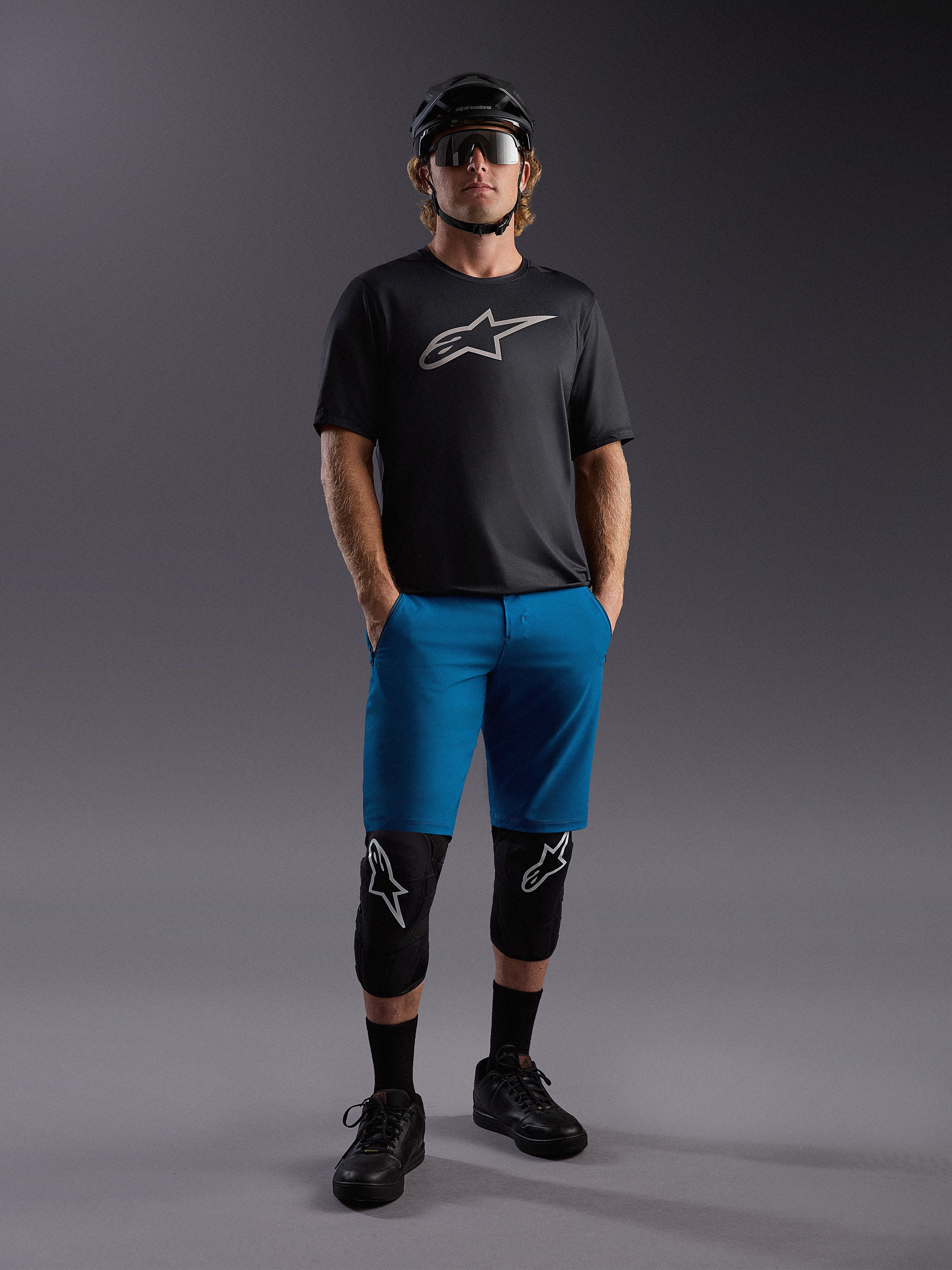 Maillot Alpinestars A-Dura Ride SS noir et short bleu, tenue de VTT complète avec protections et casque.