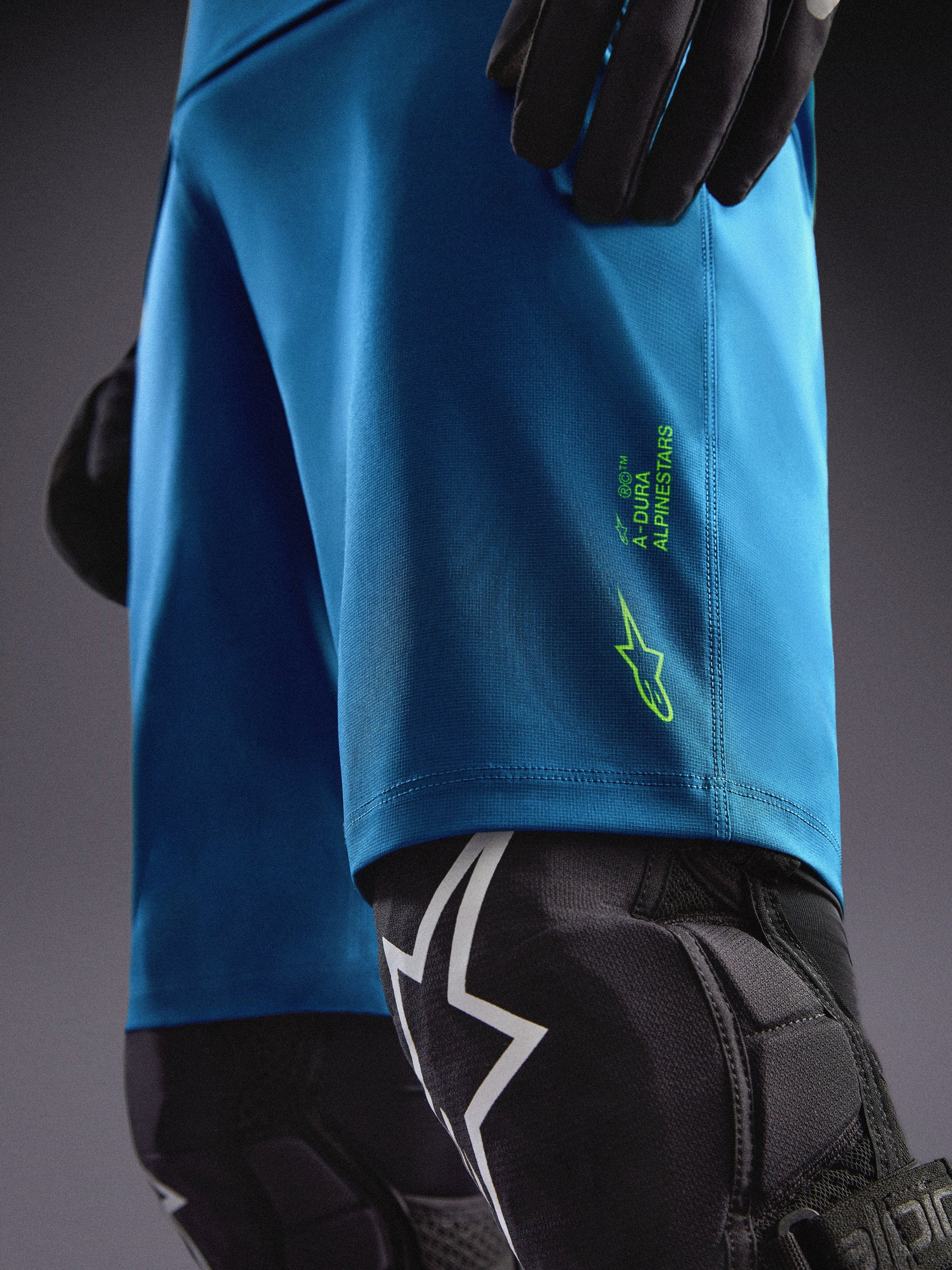 Alpinestars A-Dura Ride Shorts in Blue Green with lime green logos, paired with knee guards for MTB riding.