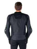Vue arrière d'un pilote portant la veste en cuir Alpinestars Missile V3 noire, dotée d'une construction en cuir premium avec des panneaux extensibles techniques, logo Alpinestars embossé dans le bas du dos et marquage discret en haut du dos, associée à un pantalon noir pour un look sportif de course coordonné.