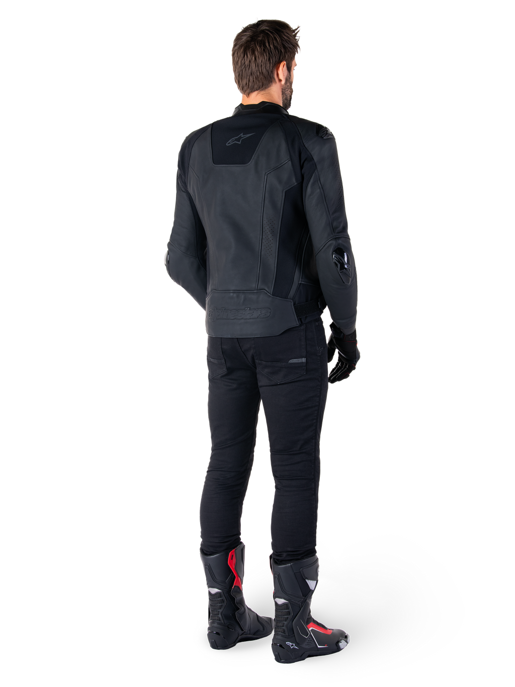 Veste en cuir Alpinestars Missile V3 noire, vue arrière sur un motard, portée avec un pantalon noir et des bottes de course noires et rouges, dotée d'une construction en cuir élégante avec un marquage ton sur ton et une coupe racing performante