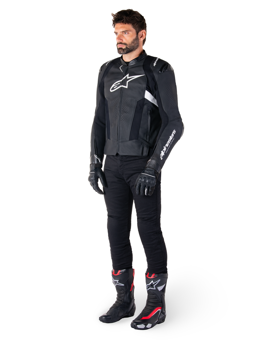 Motard portant la veste en cuir Alpinestars Missile V3 en noir et blanc, arborant un logo blanc sur la poitrine et des panneaux en cuir perforé, associée à un pantalon de moto noir, des gants noirs et des bottes de course noires et rouges pour un look de conduite sportive complet.