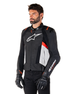 Veste en cuir Alpinestars Missile V3, noir, blanc et rouge fluo, veste de moto racing portée par un mannequin avec des gants et un pantalon noirs, dotée de panneaux en cuir perforé et d'un marquage Alpinestars distinctif