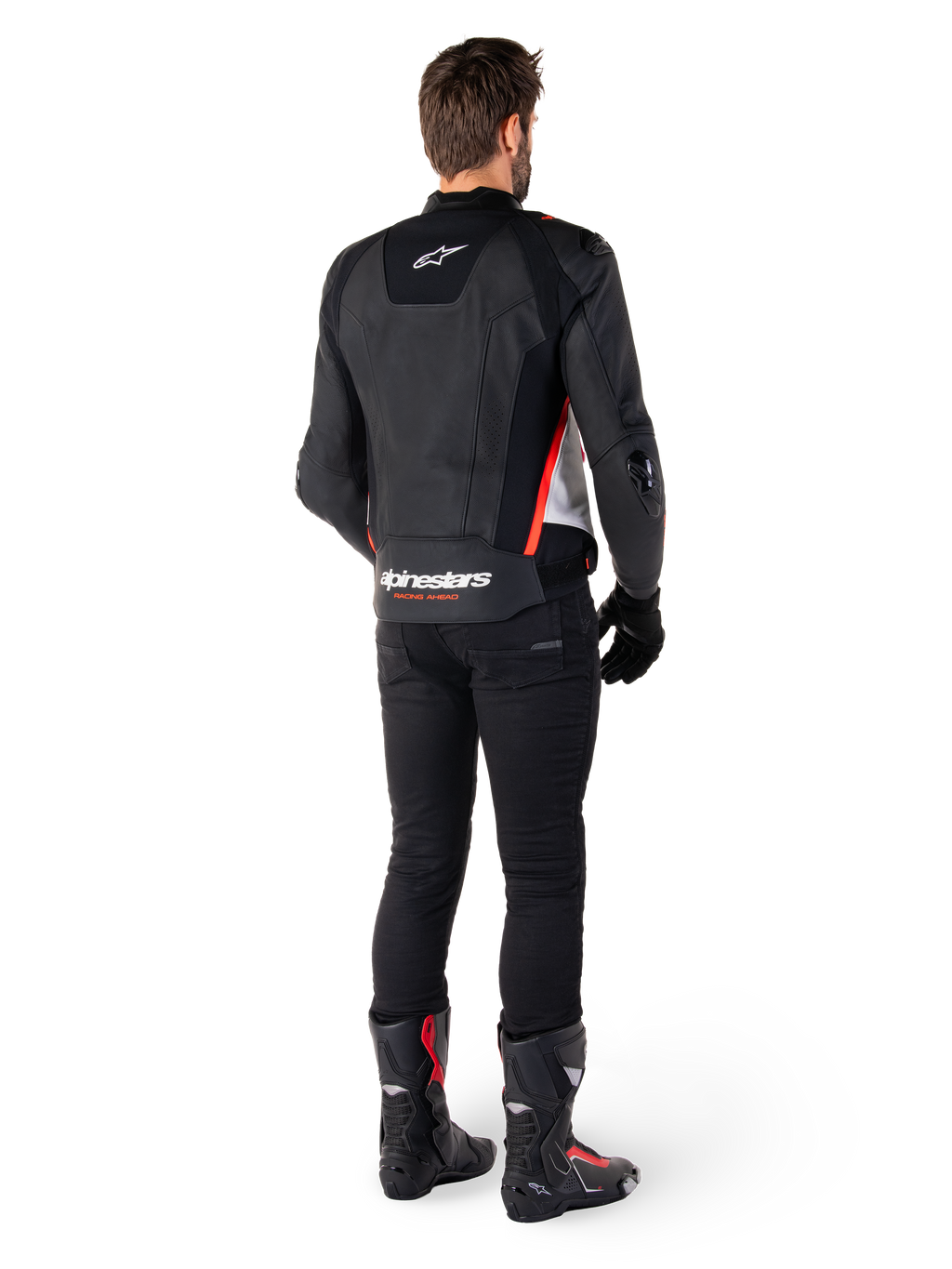 Veste en cuir Alpinestars Missile V3 en Noir Blanc Rouge Fluo, vue de dos sur un motard, arborant le logo Alpinestars sur le haut et le bas du dos, associée à un pantalon noir et des bottes de moto, veste de sport en cuir inspirée de la course