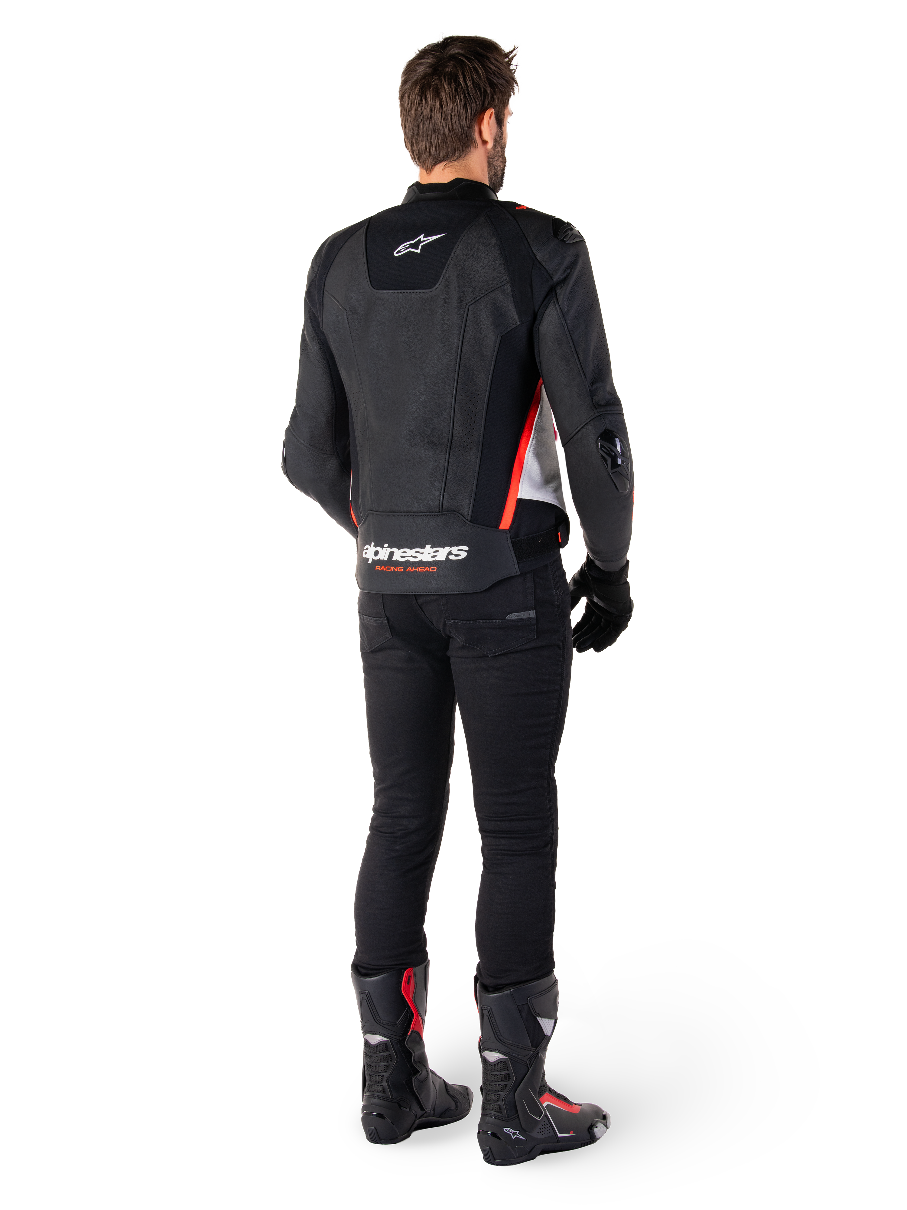 Veste en cuir Alpinestars Missile V3 en Noir Blanc Rouge Fluo, vue de dos sur un motard, arborant le logo Alpinestars sur le haut et le bas du dos, associée à un pantalon noir et des bottes de moto, veste de sport en cuir inspirée de la course