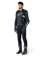 Veste en cuir Alpinestars Missile V3 Airflow, noir et blanc, portée par un mannequin homme avec un pantalon de moto noir, des gants noirs et des bottes de course avec des accents rouges et blancs, dotée de cuir perforé et de logos blancs, équipement de course de moto haute performance