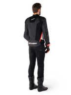 Motard vu de dos portant la veste en cuir Alpinestars Missile V3 Airflow en Noir Blanc Rouge Fluo, assortie d'un pantalon noir et de bottes noires, avec cuir perforé pour la ventilation, protections d'épaules DFS et logo Alpinestars distinctif sur le bas du dos.