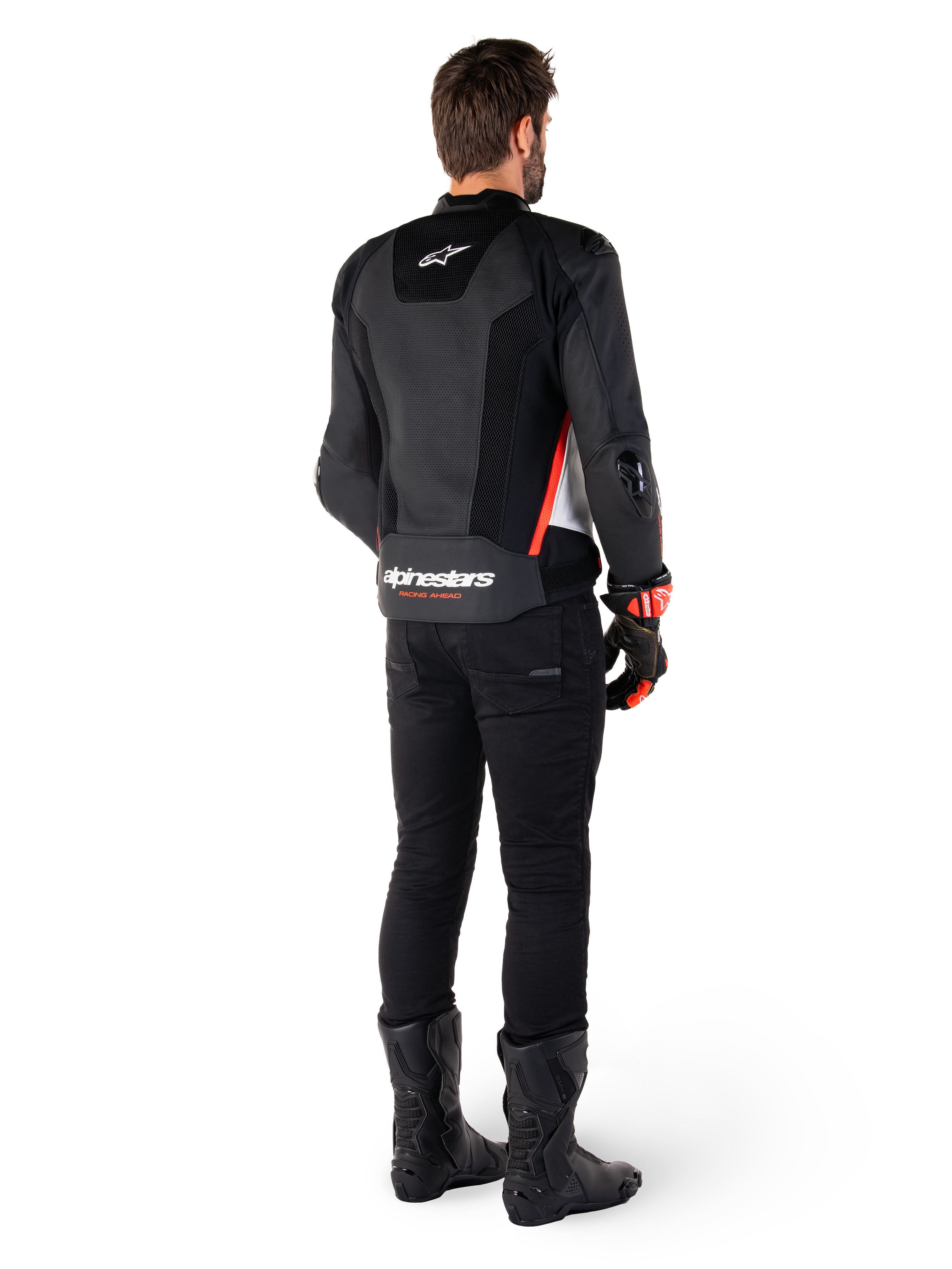 Motard vu de dos portant la veste en cuir Alpinestars Missile V3 Airflow en Noir Blanc Rouge Fluo, assortie d'un pantalon noir et de bottes noires, avec cuir perforé pour la ventilation, protections d'épaules DFS et logo Alpinestars distinctif sur le bas du dos.