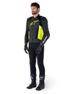 Modèle masculin portant la veste en cuir Alpinestars Missile V3 Airflow en noir, jaune fluo et blanc, associée à des gants, un pantalon et des bottes de moto noirs, mettant en valeur la conception en cuir perforé et l'esthétique inspirée de la course.