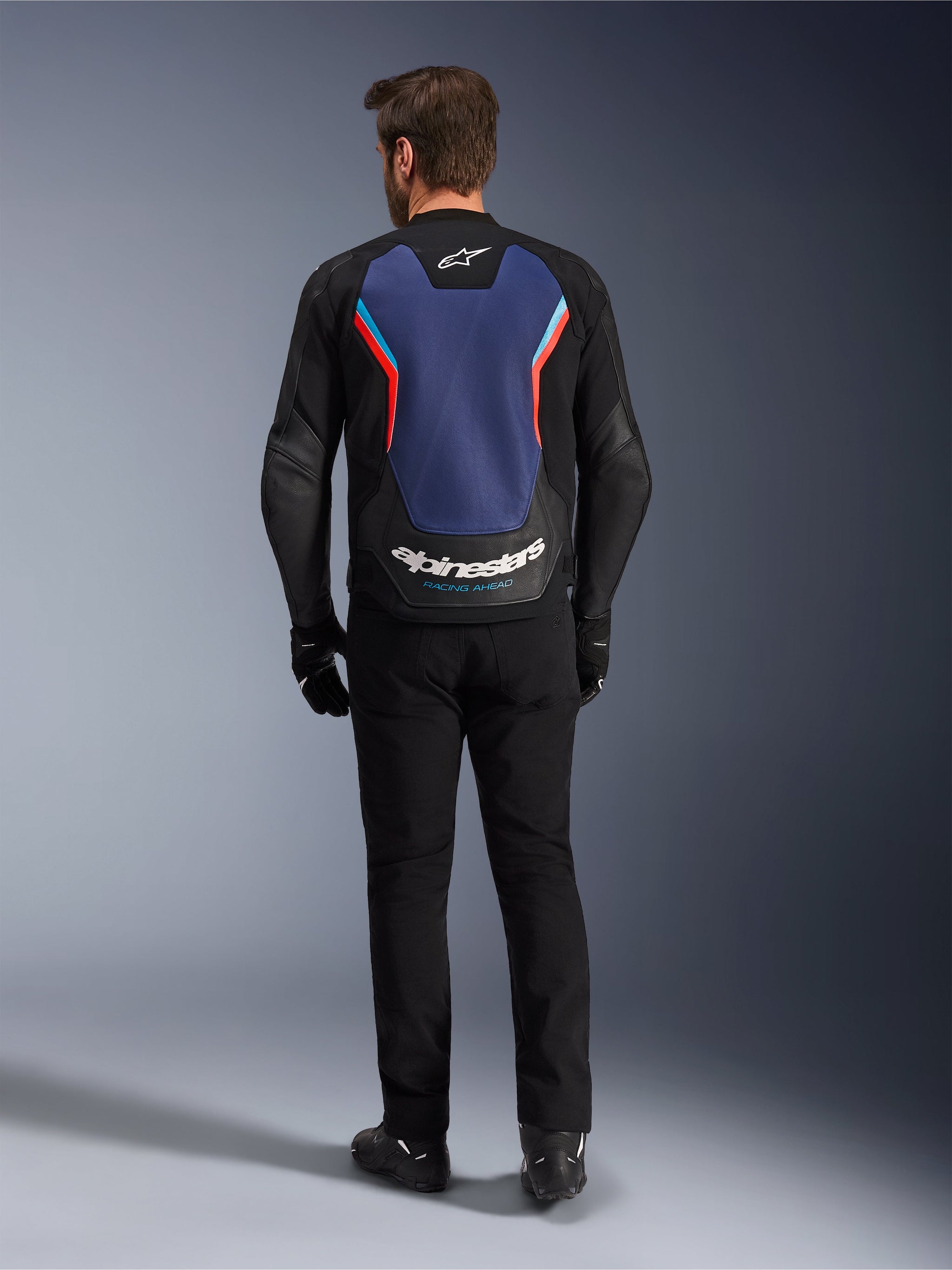 Blouson en cuir Alpinestars GP Force V2, blouson de moto sport, Noir Bleu Rouge Fluo, vue de dos sur un mannequin, présentant un large panneau dorsal bleu avec des accents rouges et bleu clair et le logo Alpinestars blanc en bas du dos, associé à un pantalon et des gants de moto noirs.