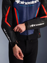 Blouson en cuir Alpinestars GP Force V2 en noir, bleu et rouge fluo, vue rapprochée d'une personne ajustant la fermeture éclair du poignet, arborant des logos Alpinestars blancs sur l'avant-bras et la poitrine, construction en cuir bovin texturé pour la conduite de moto sportive