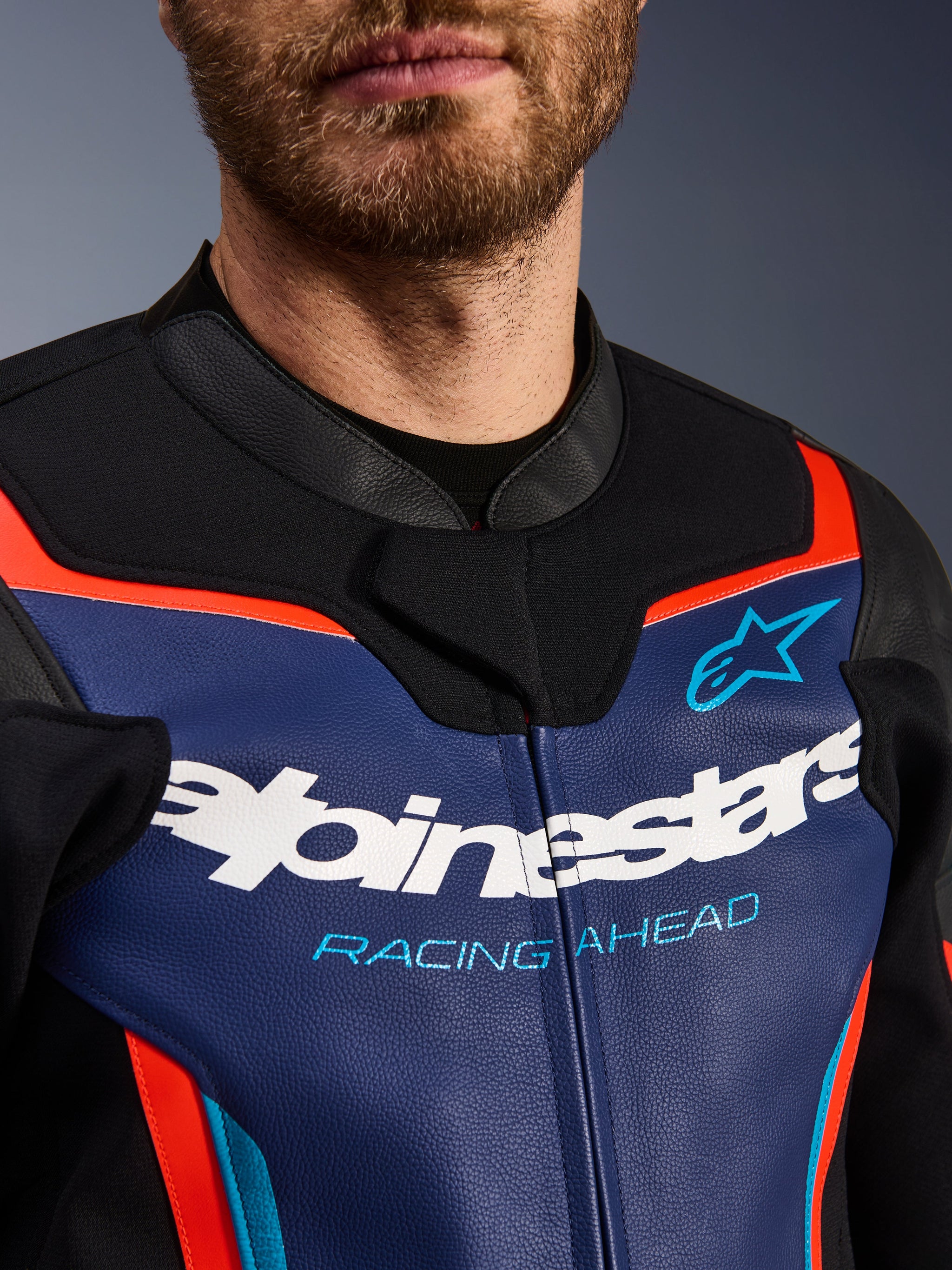 Blouson en cuir Alpinestars GP Force V2, vue détaillée de la poitrine et du col, bleu, noir et rouge fluo, avec logo Alpinestars blanc et inscription « RACING AHEAD » bleu clair, texture de cuir premium avec accents fluorescents
