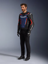 Modèle portant le blouson en cuir Alpinestars GP Force V2 en noir, bleu et rouge fluo, associé à un pantalon de moto technique noir, des gants noirs et des bottes, équipement de moto professionnel pour la conduite sportive