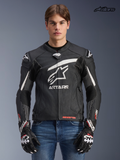 Alpinestars Veste En Cuir GP Plus R V4 Rideknit, veste de moto racing pour homme noire et blanche, vue de face sur un modèle portant des gants assortis et un jean