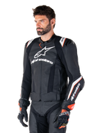 Modèle masculin portant la veste en cuir Alpinestars Missile V3 Ignition, noir avec des accents blancs et orange, dotée de logos blancs distinctifs, de sections en cuir perforé et de protections d'épaules, avec des gants de course pour un look sport-racing.