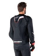 Veste en cuir Alpinestars Missile V3 Ignition, vue arrière, noir avec accents blancs et rouges, dotée d'une bosse aérodynamique sport et du logo Alpinestars, portée avec un pantalon en cuir assorti et des gants de course