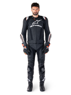 Pilote portant la veste en cuir Alpinestars Missile V3 Ignition en noir, associée à un pantalon en cuir, des gants et des bottes assortis, avec logos Alpinestars blancs et accents rouges, conçue pour la performance de course professionnelle.