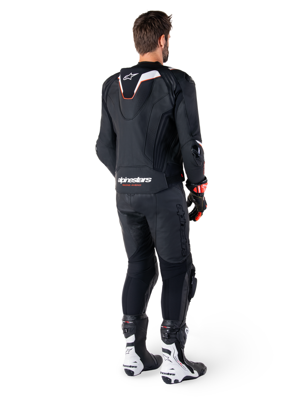 Vue arrière d'un pilote portant la veste en cuir Alpinestars Missile V3 Ignition noire, avec une bosse aérodynamique sport aux accents blancs et rouges, marquage Alpinestars au bas du dos, associée à un pantalon en cuir noir et des bottes de course noires et blanches, tenue de pilotage sportive professionnelle
