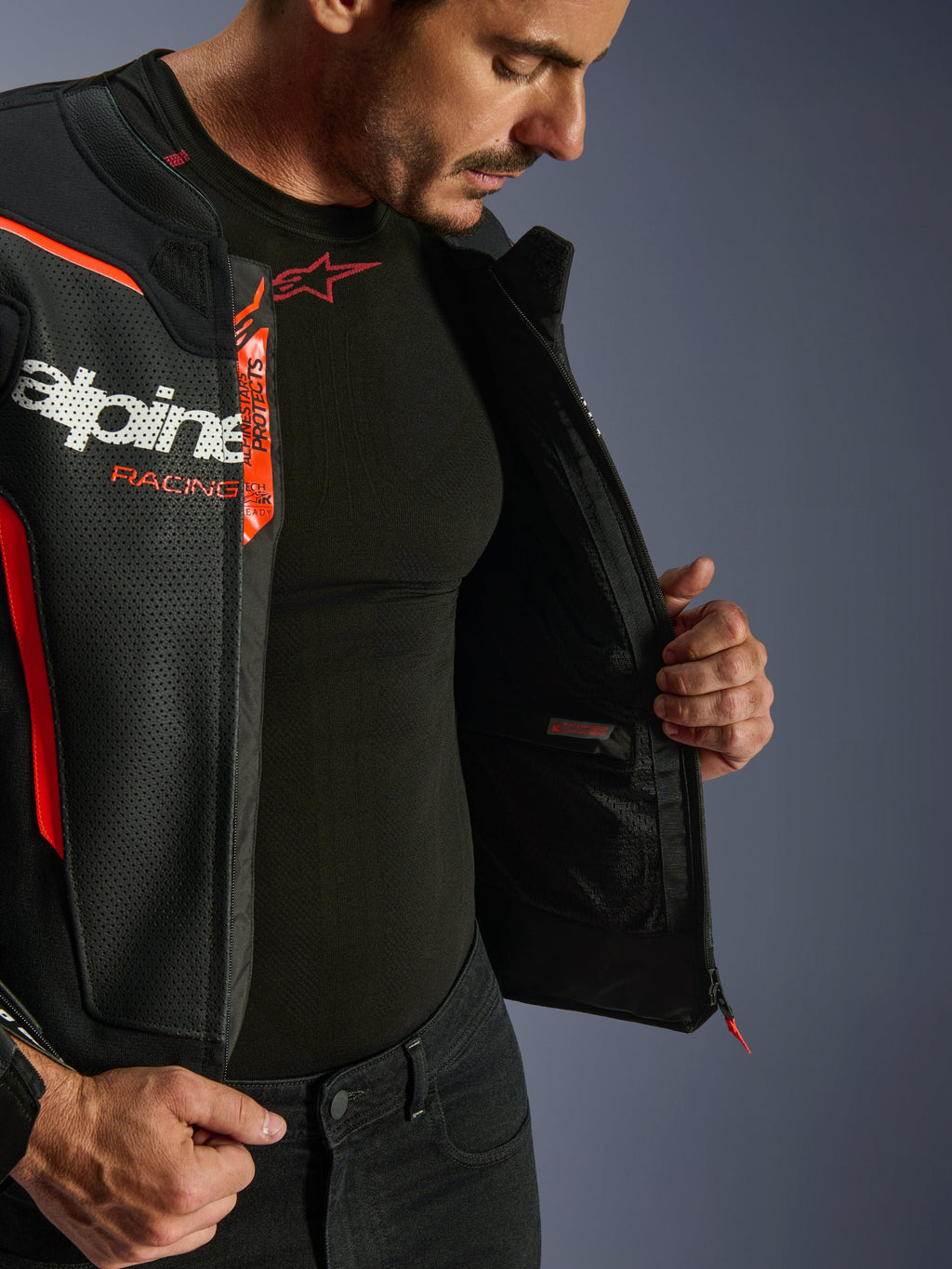 Blouson en cuir Alpinestars GP Force V2 Air, noir et rouge fluo, ouvert pour révéler une poche intérieure imperméable et les logos, construction multi-panneaux en cuir perforé pour la circulation de l'air, porté avec une sous-couche Alpinestars noire.
