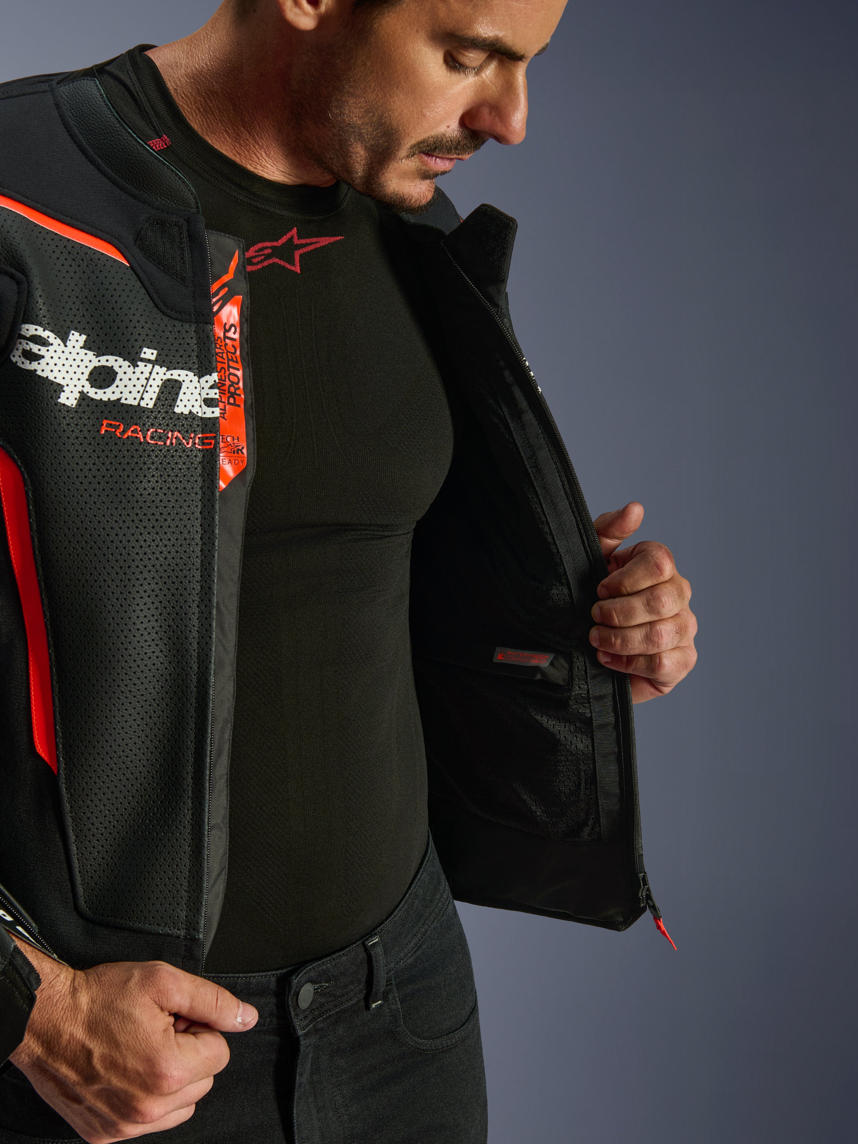 Blouson en cuir Alpinestars GP Force V2 Air, noir et rouge fluo, ouvert pour révéler une poche intérieure imperméable et les logos, construction multi-panneaux en cuir perforé pour la circulation de l'air, porté avec une sous-couche Alpinestars noire.