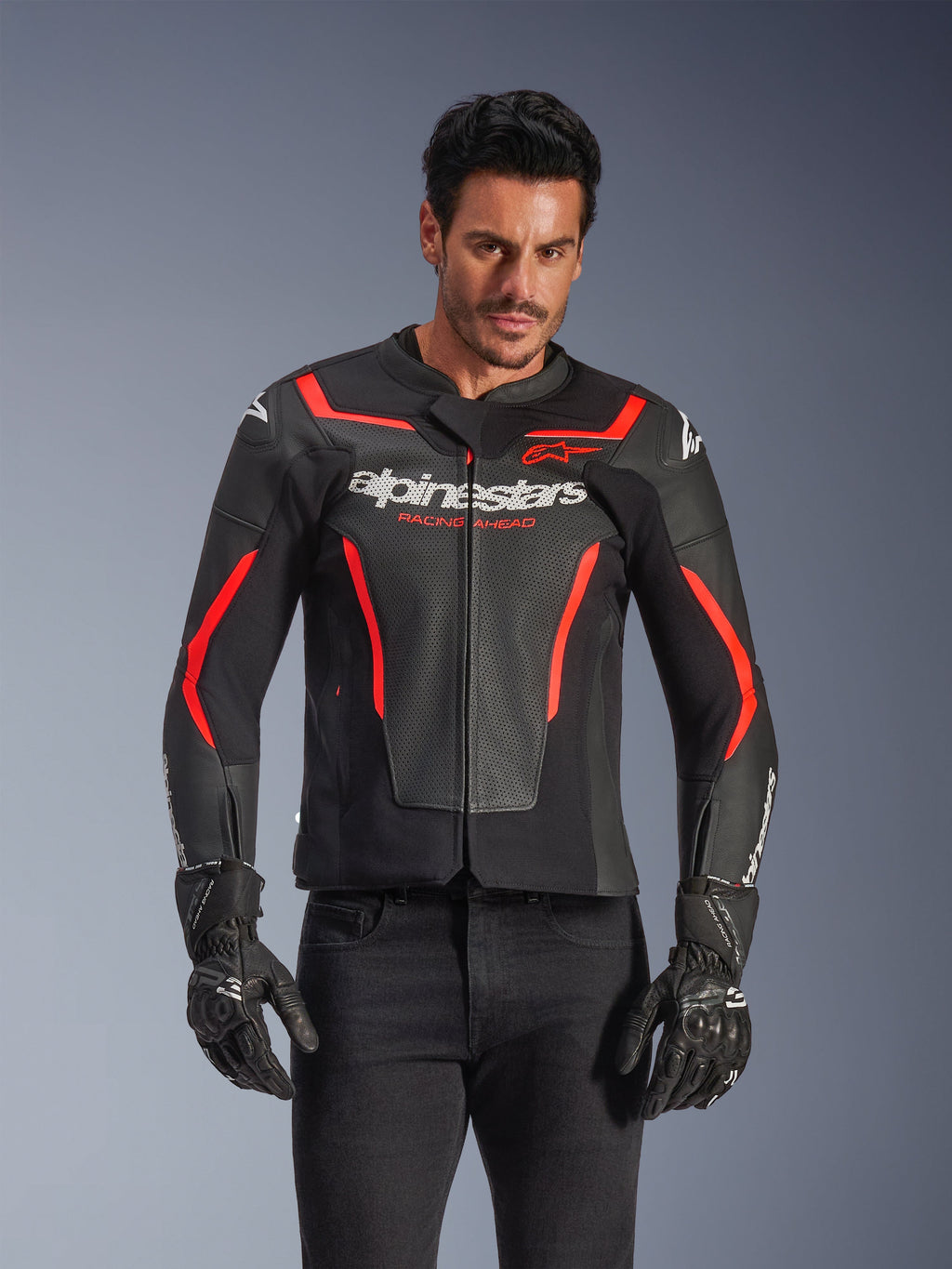 Blouson en cuir Alpinestars GP Force V2 Air, veste de moto de course, noir et rouge fluo, construction en cuir de qualité supérieure avec de larges perforations pour la circulation de l'air, porté par un mannequin avec gants et pantalon noirs, arborant un logo imposant et l'inscription 'Racing Ahead' sur la poitrine