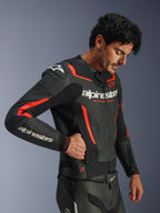 Blouson en cuir Alpinestars GP Force V2 Air, noir et rouge fluo, blouson de moto en cuir perforé, mannequin portant le blouson et mettant la main dans une poche latérale zippée, avec des accents rouge fluo et logos Alpinestars blancs, équipement de conduite sportive professionnel