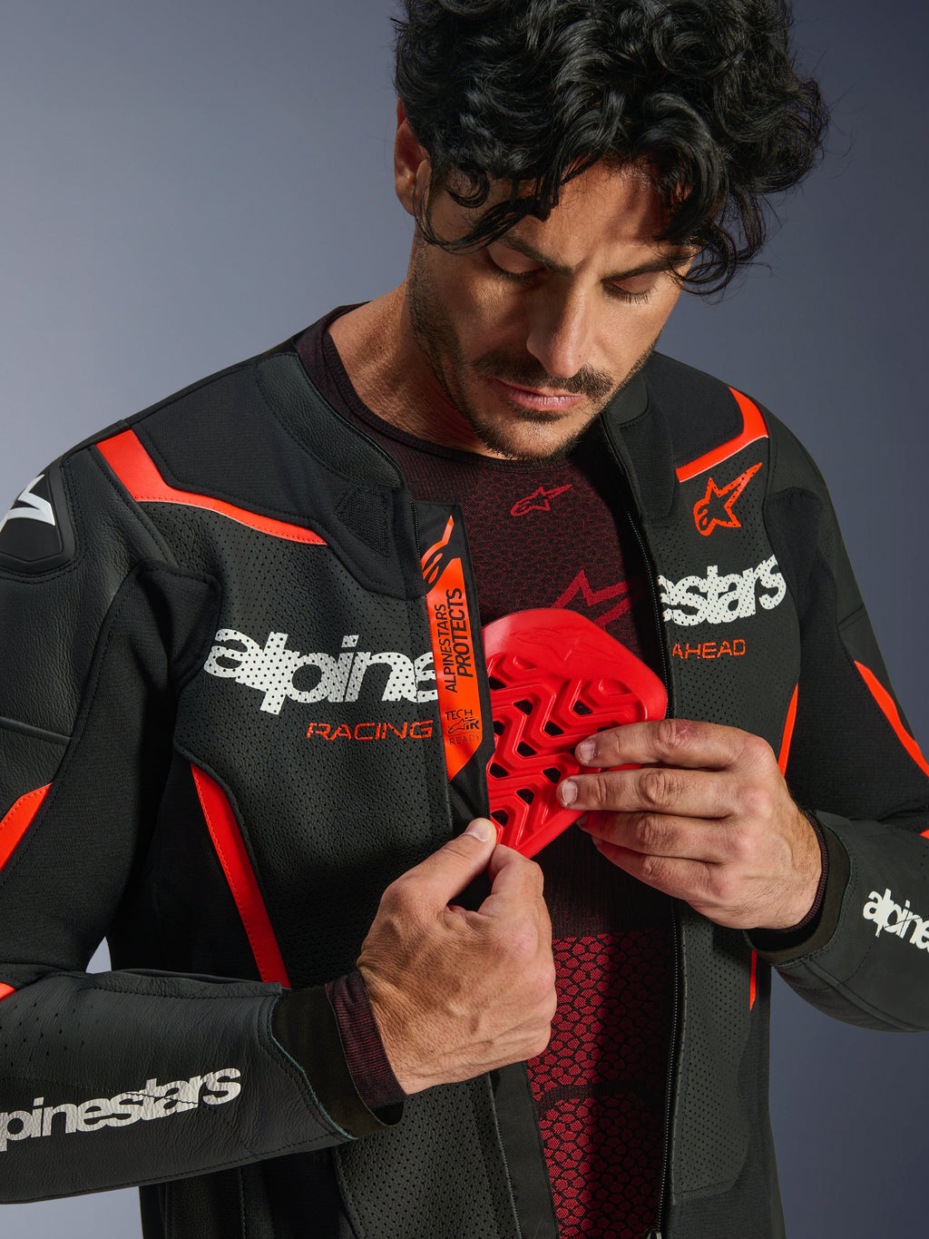 Blouson en cuir Alpinestars GP Force V2 Air en Noir et Rouge Fluo, homme ouvrant le blouson pour révéler l'insertion d'une protection de poitrine rouge, avec cuir perforé, logos blancs et détail Tech-Air Ready sur le rabat interne